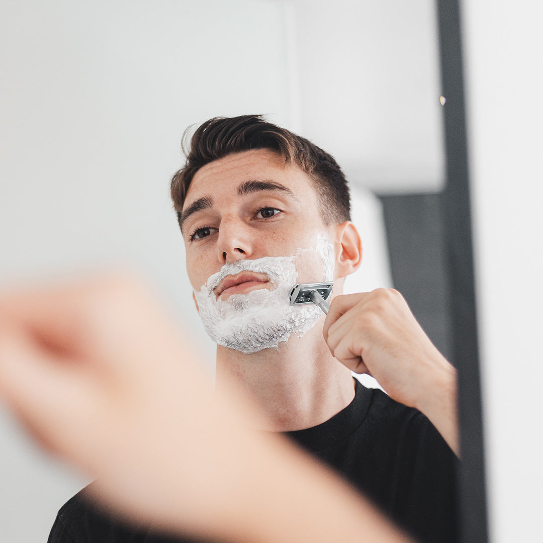 man shaving face in mirror with facial lather